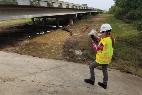 Inspector at a bridge site entering information on a tablet.