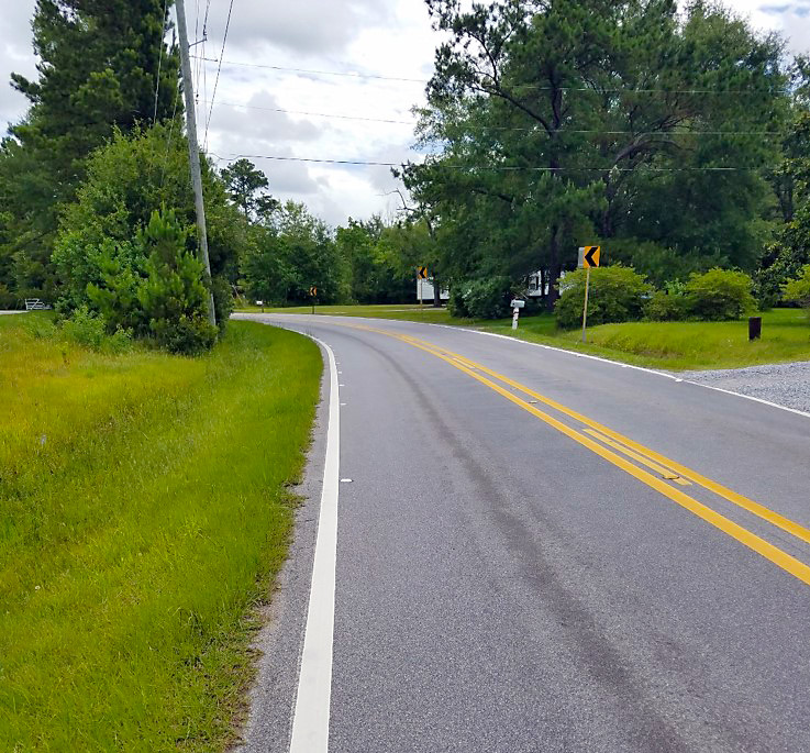 Road with chevron sign, centerline and edge striping, and gravel edge treatment.