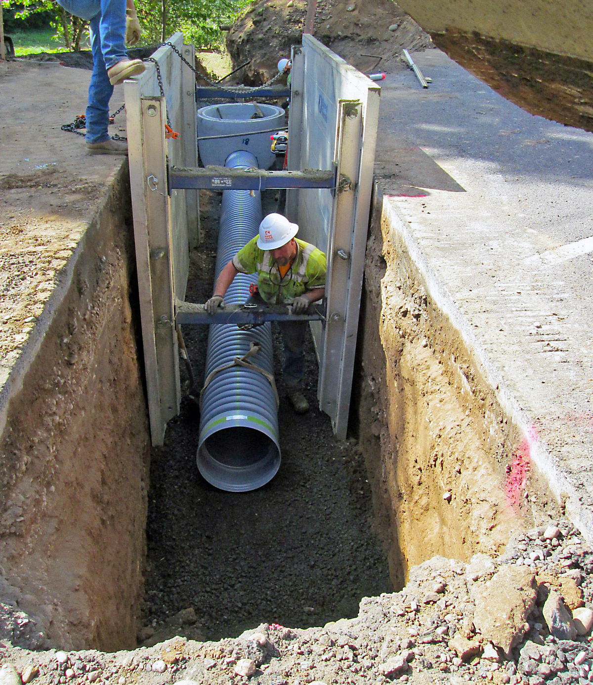 Two construction workers install a new culvert under a highway.