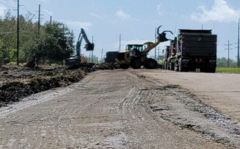excavator clearing roadside and tractor dumping debris into dump truck
