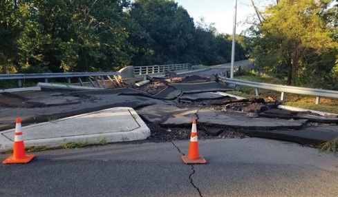 asphalt road, severely damaged from flooding and marked with orange safety cones