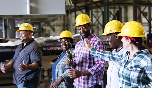 Row of happy workers, smiling, with hard hats on in a factory.