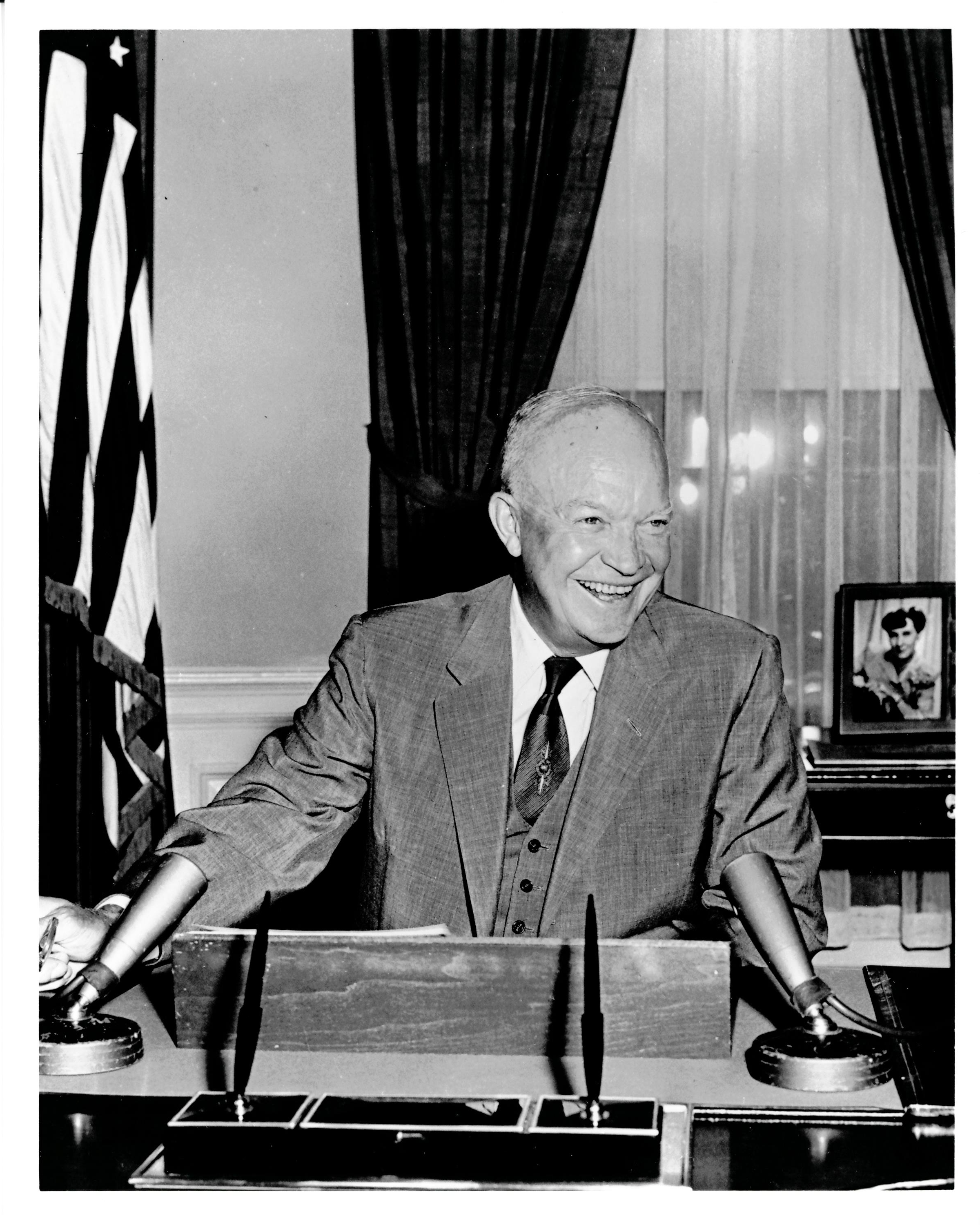 President Dwight D. Eisenhower smiling and sitting at a desk.