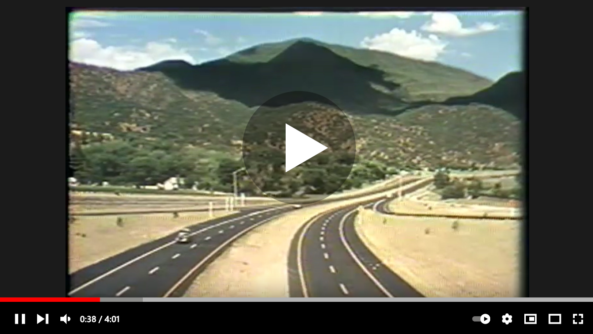 A media play button and controls over a still image of a scenic highway with mountains in the background.