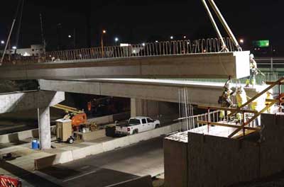 Photo. Nighttime image of a girder being lowered onto concrete support towers.