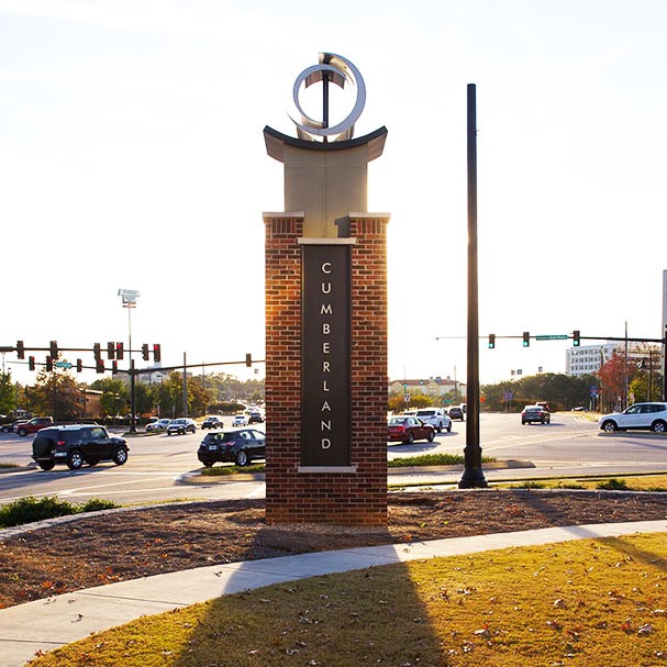A busy intersection with a brick monument displaying 'Cumberland' in the foreground.