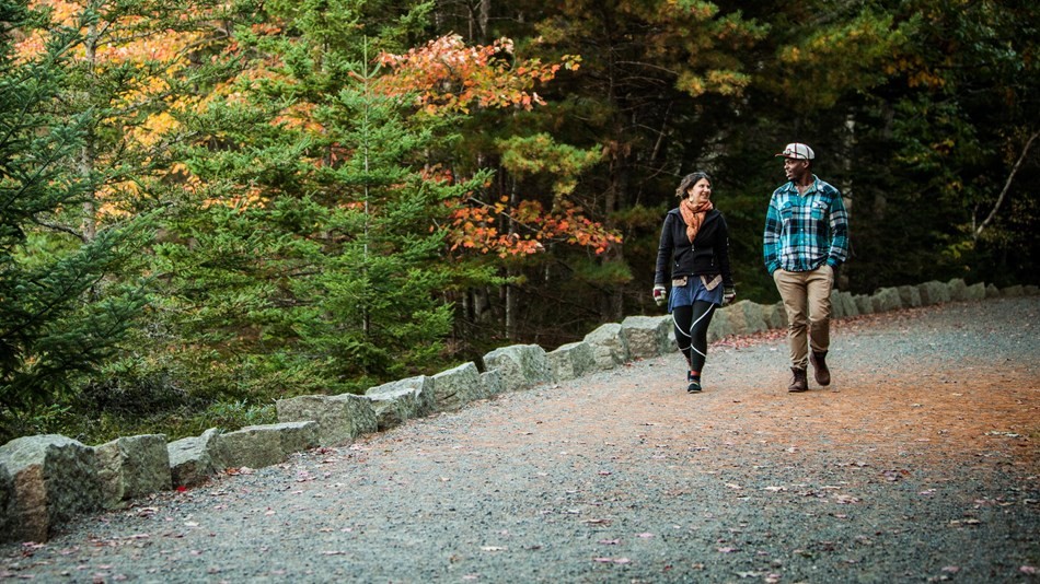 Woman and man walk along gravel carriage road under fall colors.