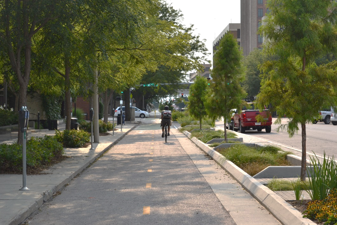 The photo highlights the landscaping along the bikeway.