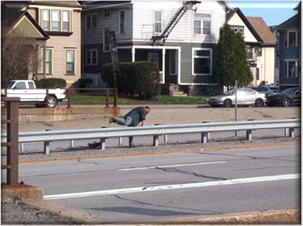 A man is climbing over a guardrail which separates the expressway from a nearby neighborhood, demonstrating how the expressway is a barrier to neighborhood connectivity.