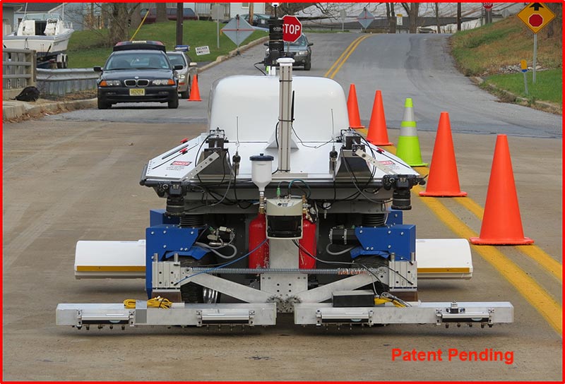 A photograph of the RABITTM Bridge Deck Assessment Tool appears in the center of the slide. RABIT stands for the Robotic Assisted Bridge Inspection Tool. The front mechanical arms of the RABITTM Bridge Deck Assessment Tool are visible and contain equipment for electrical resistivity tests (Wenner probes), and two acoustic arrays for impact echo tests and ultrasonic surface wave tests. Two high-resolution cameras pointed down at the bridge deck are also attached to the front of the robot. One GPS antenna is also visible at the top of the robot. The RABIT™ Bridge Deck Assessment Tool is situated on a two-lane bridge. Four orange and one yellow-green cone are set up on the double yellow line to keep traffic from the RABIT™ Bridge Deck Assessment Tool. There are three cars behind the tool. A text box with text in it appears to the left of the image. A photograph of the RABITTM Bridge Deck Assessment Tool appears in the center of the slide. RABIT stands for the Robotic Assisted Bridge Inspection Tool. The front mechanical arms of the RABITTM Bridge Deck Assessment Tool are visible and contain equipment for electrical resistivity tests (Wenner probes), and two acoustic arrays for impact echo tests and ultrasonic surface wave tests. Two high-resolution cameras pointed down at the bridge deck are also attached to the front of the robot. One GPS antenna is also visible at the top of the robot. The RABIT™ Bridge Deck Assessment Tool is situated on a two-lane bridge. Four orange and one yellow-green cone are set up on the double yellow line to keep traffic from the RABIT™ Bridge Deck Assessment Tool. There are three cars behind the tool. A text box with text in it appears to the left of the image.