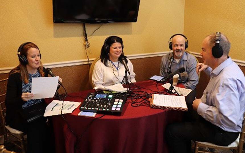 4 people at a table with sound equipment, recording a podcast