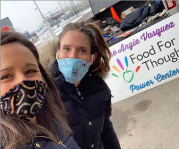 Two masked volunteers in front of a Food for Thought banner.