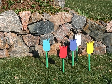 Painted wooden tulips planted in grass next to a stone wall.