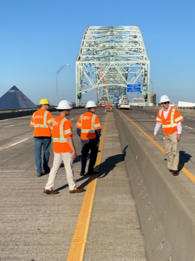Group of people wearing safety jackets and hard hats inspecting a bridge.