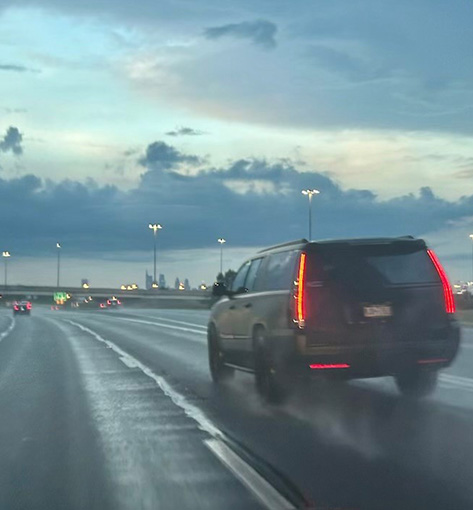 An SUV driving in the middle lane on a 6-lane highway on very wet pavement conditions.