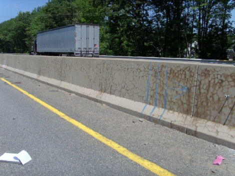 This image shows a section of stained, cracked concrete barriers. Three lines and an arrow that have been spray-painted on the surface is visible, and is shown to separate two areas of the barrier section. The barriers to the right of the lines show more cracking than the barriers located to the left of the lines.