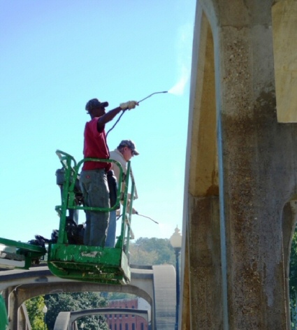 This image shows two workers topically applying a material on a concrete bridge element.
