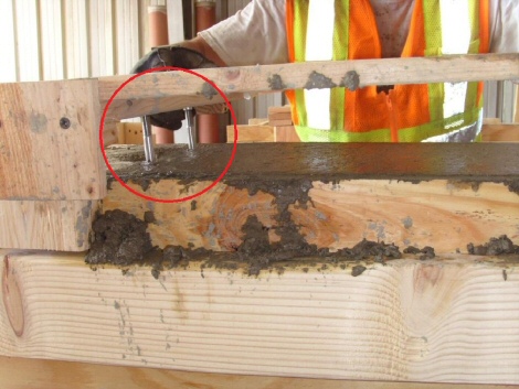 This image shows a worker placing steel pins into the surface of a fresh concrete blocks. The steel pins are held by wooden formwork that fits perfectly on top of the fresh concrete block.