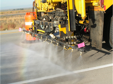 Topical application on I-84. This photo shows a closeup view of a water truck spraying lithium nitrate on an A S R-affected pavement near Mountain Home, Idaho.