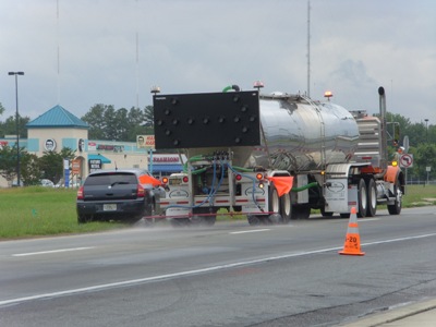 This image shows a large truck with an unlit arrow sign mounted on the back spraying a section of pavement with lithium nitrate solution.