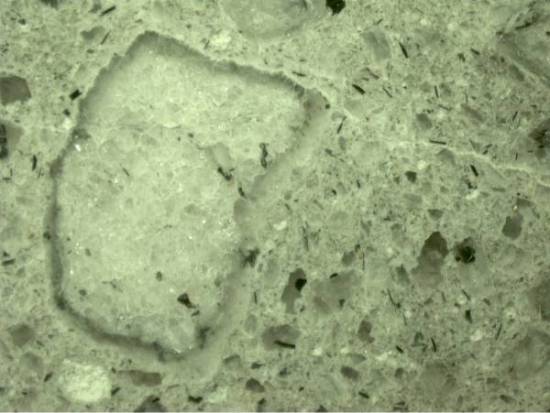This image shows a microscopic view of a concrete sample. On the left hand side of the image is a large aggregate particle with a reactive gel surrounding the aggregate.