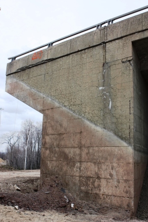 This image shows a concrete bridge wall, where half of the structure has been excavated. Cracking can be seen above the line where the structure was exposed to the environment. The section that was buried shows no sign of cracking.