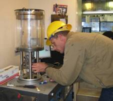 Alan Spivey, a technician on the FHWA Mobile Asphalt Material Testing Laboratory, prepares a specimen for testing in the Asphalt Mixture Performance Test system.