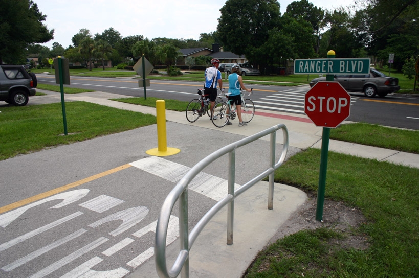 Two bicyclists on a bike trail wait to cross Ranger Boulevard in Orlando, Florida.