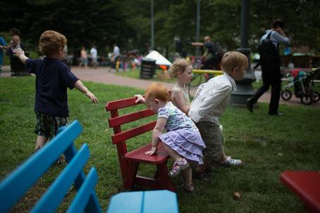 Children playing and climbing on a bench in a park.