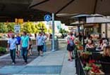 Groups of people walking along the ICT. To the right of the trail, customers are dining underneath umbrellas at a sidewalk café.