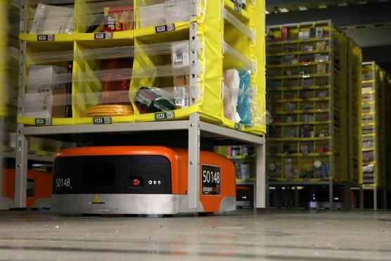 Photo of small robotic machine lift and moving a set of products across the floor in the Amazon fulfillment center.