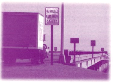 Picture of a truck heading across a roadway with a sign reading Patrolled for Your Safety on the right side of the road.