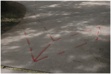 Examples of Inductance Loop Detector Shapes for Bicyclist Counting (Double Chevron Shape: Photo). This photo shows an installed double chevron loop with spray paint used to highlight the cuts in the surface.