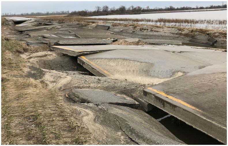 Damaged section of US 34 exhibiting cracked pavement, washed out embankment, and displacement of the roadway.