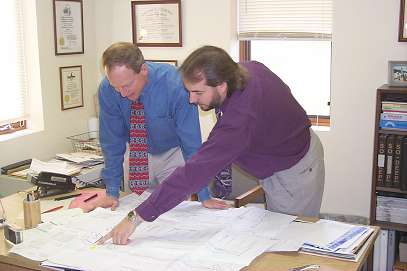 Photo: Two men working at a desk with plans. Saying: I think the gas line in here, but I'm not really sure. It might be in conflict with this proposed piling. I guess we'll let the contractor worry about that.