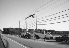 Photo at a distance of utility vehicle and worker working on utility pole