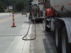Figure 7. Photo. Diamond grinding on U.S. 23. Diamond grinding is performed on the longitudinal construction joint in the left wheel path of a bridge deck on U.S. 23 in southern Ohio. Two trucks and a traffic cone are visible.