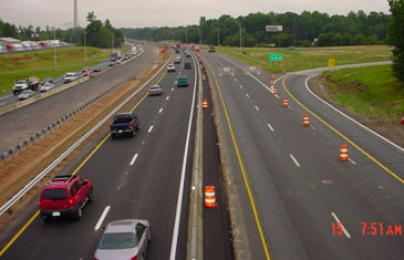Photo. Highway work zone. A work zone is set up in two lanes on the right-hand side of a highway, with traffic traveling in two lanes on the left-hand side. Orange cones separate the left-hand lanes from the work zone.