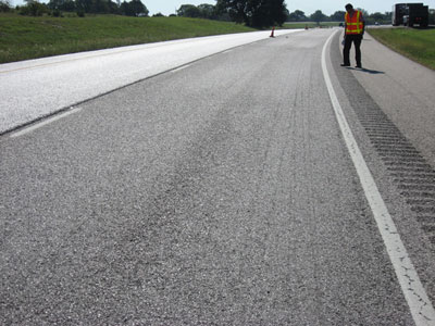 Photo. A scanning tour team member examines an ultrathin bonded wearing course on I-10 near San Antonio, TX. The photo shows a close-up view of the asphalt pavement.