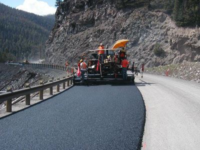 Figure 4. Photo. A work crew places warm-mix asphalt on Yellowstone National Park's East Entrance Road. A paver can be seen with three workers on it.