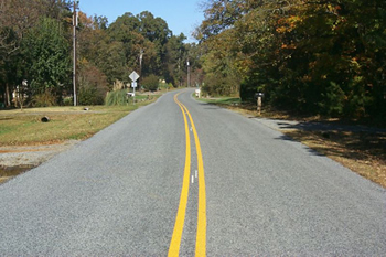 Figure 5. Photo. Two-lane road, divided by double solid yellow lines, winding through rural wooded area.