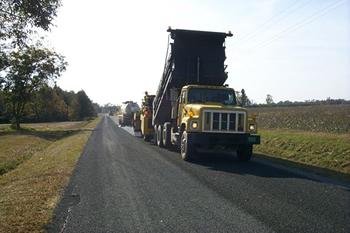  Figure 4. Photo. A dump truck deposits its load on a country road as other construction vehicles prepare for road maintenance.