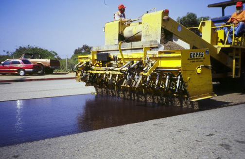 Figure 1. Photo. A close-up view of a chip seal being applied to a roadway.