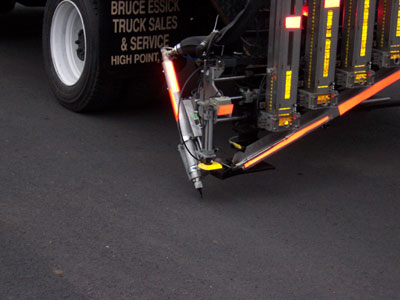 Figure 2. Photo. A close-up of the Automated Roadway Pavement Marker Placement System as it applies pavement markers to the roadway.