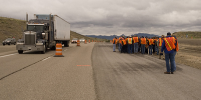 Figure 5. Photo. Participants at the Western Region In-Place Recycling Workshop visit a cold in-place recycling project on I-80 in Pequop, Nevada. Participants wearing safety vests stand on the side of I-80 while a tractor-trailer truck and cars pass by.