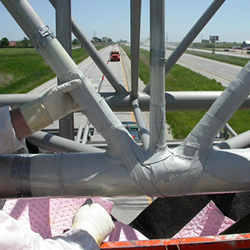 Figure 5. Photo. A close-up of fiber-reinforced polymer composite wraps being applied to an overhead sign structure.
