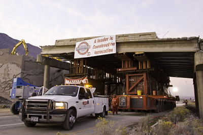 Figure 2. Photo. The old 4500 South bridge is removed using a self-propelled modular transporter (SPMT). The bridge is jacked up on the SMPT and a truck is in front of the SPMT.