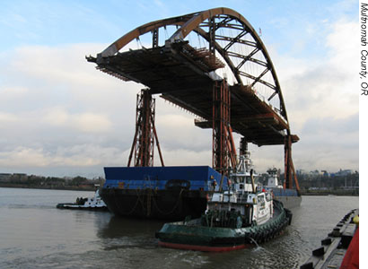 Figure 7. Photo. The Sauvie Island bridge in Multnomah County, OR, is transported by barge down the Columbia River.