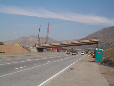 Figure 1. Photo. A view of the completed 4500 South bridge in Salt Lake City, UT. Traffic is traveling under the bridge. Two construction cranes are visible.