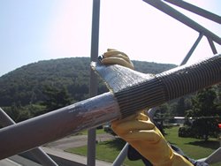 Figure 6. Photo. A close-up view of two gloved hands wrapping an overhead sign structure with fiber-reinforced polymer composites. 